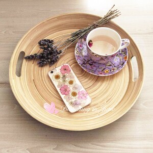 May include: A round wooden tray with a purple floral teacup and saucer, a bunch of lavender, and a phone case with pressed flowers.