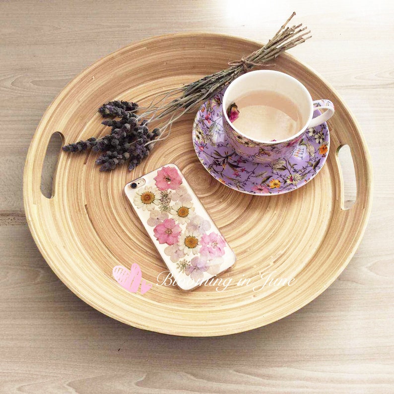 May include: A round wooden tray with a purple floral teacup and saucer, a bunch of lavender, and a phone case with pressed flowers.