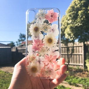 May include: A clear phone case with pressed pink and white flowers. The flowers are arranged vertically in a cascading pattern.