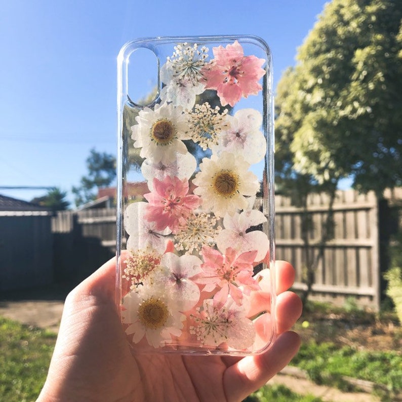 May include: A clear phone case with pressed pink and white flowers. The flowers are arranged vertically in a cascading pattern.