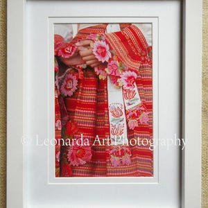 May include: A close-up of a red and white embroidered fabric with floral designs. The fabric is folded in half and the embroidery is visible on both sides.