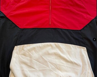 Puede incluir: Una chaqueta cortavientos de color rojo, negro y crema con cierre de cremallera. La chaqueta tiene un cuello alto y un bolsillo canguro.