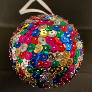 Peut inclure: Une boule de Noël ronde recouverte de paillettes colorées. Les paillettes sont dans des tons de rouge, vert, bleu, or, argent et rose.