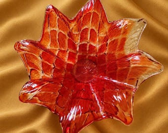 May include: A star-shaped glass bowl featuring a vibrant red and orange color gradient. The surface displays a textured, grid-like pattern of raised lines that radiate from the center toward the pointed edges of the bowl, creating a translucent effect.