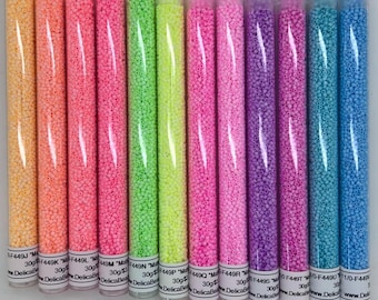 May include: A collection of colorful seed beads in clear plastic tubes. The beads are in shades of yellow, orange, pink, green, purple, and blue. Each tube is labeled with a product code and weight. These beads are ideal for jewelry making and crafting.