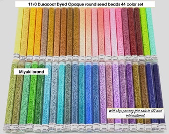 May include: A set of 44 colors of 11/0 size Miyuki Duracoat Dyed Opaque round seed beads in small glass vials. The beads are arranged in rows by color, with a variety of shades from yellow to purple.