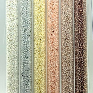 May include: Set of six 11/0 seed beads in alabaster neutral pastel colors. The colors are white, silver, cream, pink, beige, and brown. The beads are packaged in small clear tubes with labels that include the bead size, color number, and website address.