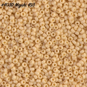 May include: A close-up image of a large quantity of small, round, cream-colored beads. The beads are arranged in a random pattern and are all the same size. The text #403D Miyuki 493 is visible in the top left corner of the image.
