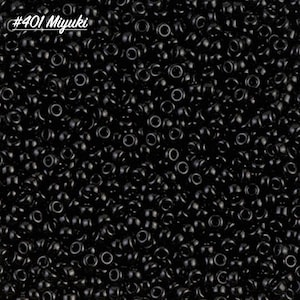 May include: A close-up image of a large quantity of small, black, round seed beads. The beads are arranged in a random pattern and appear to be made of glass or plastic. The beads are commonly used for jewelry making and other craft projects.