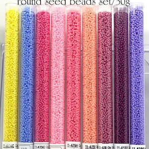 May include: A collection of 11/0 Op Hawaiian Sunset round seed beads in clear tubes. The tubes display beads in various colors, including yellow, blue, pink, peach, and purple. Each tube is labeled with a product code and price.