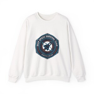 May include: White crewneck sweatshirt with a circular graphic. The graphic features a rocket ship design with the text "DEEP SPACE SURVIVAL TEAM SYSTEMS ONLINE" in a blue and red color scheme. The sweatshirt is a casual style.