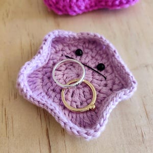 Pode incluir: Um prato em forma de estrela de crochê roxo com dois anéis dentro. O prato tem dois botões pretos para os olhos.