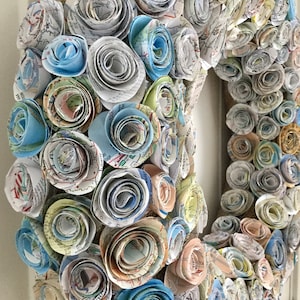 May include: A wreath made of paper roses, each rose is made from a map, the roses are in shades of blue, green, and brown.