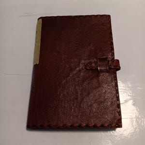 May include: A brown leather-bound journal with a stitched edge and a leather strap closure.