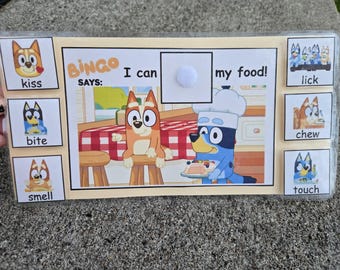 May include: A Bluey Bingo game featuring character illustrations. The game includes the text "BINGO SAYS: I can my food!" and images with words such as "kiss", "bite", "smell", "lick", "chew", and "touch".