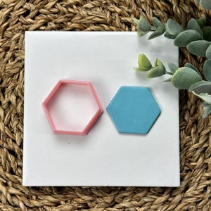 May include: Two hexagon-shaped cookie cutters, one pink and one blue, on a white background.