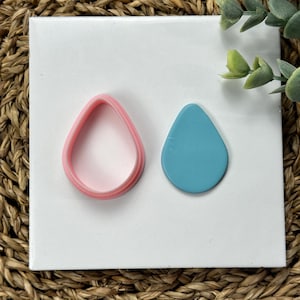 May include: Two teardrop-shaped polymer clay earrings, one pink and one blue. The pink earring is a layered cutout, while the blue earring is solid.