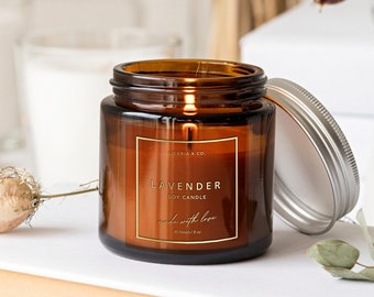 May include: A brown glass jar candle with a gold label that reads "Lavender Soy Candle" and "Made with love". The candle is lit and the jar has a silver lid.