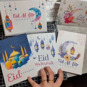 May include: Four greeting cards with watercolor illustrations of crescent moons, stars, lanterns, and mosques. The cards feature the text "Eid Mubarak" and "Eid Al-fitr Mubarak".