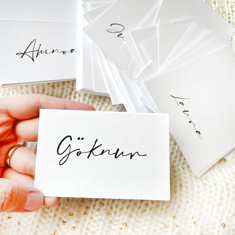 May include: A stack of white cards with black calligraphy. The top card reads "G&ouml;knum".