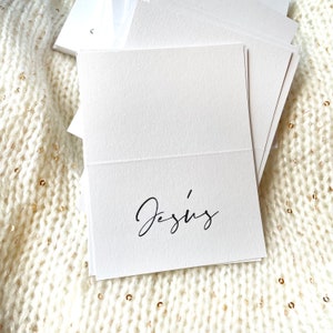May include: White place card with the name "Jesus" written in black cursive script.