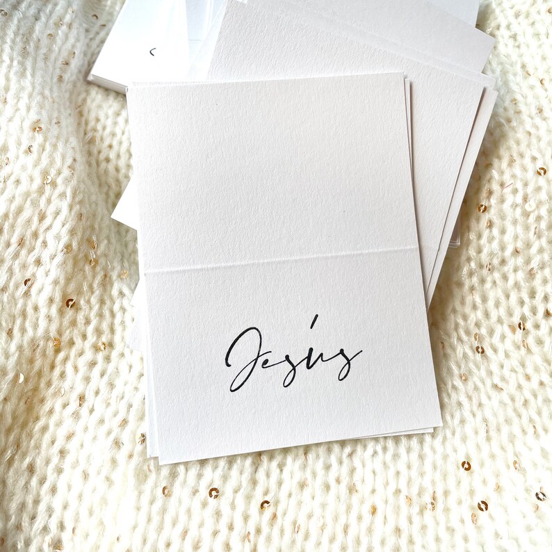 May include: White place card with the name "Jesus" written in black cursive script.