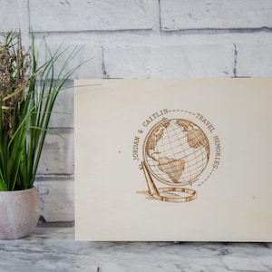 Puede incluir: Una caja de madera con un diseño de globo terráqueo y el texto "Jordan & Caitlin - Travel Memories".