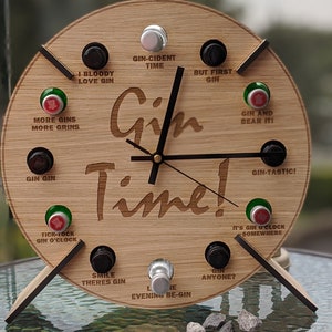 May include: A wooden clock with a gin theme. The clock face has a black hand and a gold hand. The clock face has a variety of phrases related to gin, such as "Gin-cident Time", "I Bloody Love Gin", and "Gin and Bear It".