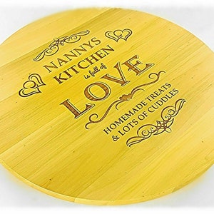 May include: A round wooden chopping board with the text "Nanny's Kitchen is full of Love, Homemade Treats & Lots of Cuddles" engraved on it.