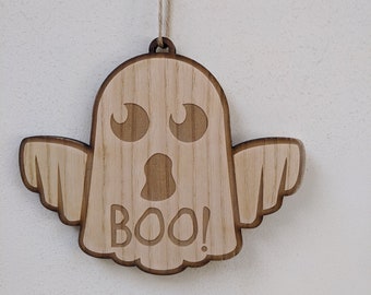May include: A wooden ghost ornament with a friendly face and the word "BOO!" carved into it. The ornament is hanging from a string.