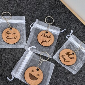 May include: Four wooden keychains with different messages and a smiley face design. The keychains are packaged in individual clear organza bags.