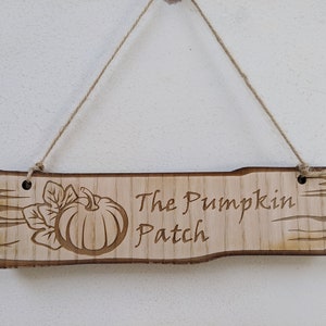May include: A wooden sign with a rustic, weathered look, featuring a carved pumpkin and the text "The Pumpkin Patch". The sign is hanging from a twine string.
