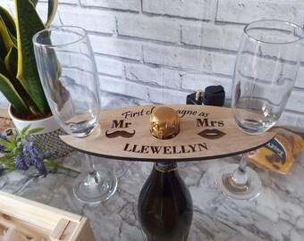 May include: Wooden champagne holder with two glass flutes, a bottle of champagne, and the text "First of agne as Mr Mrs LLEWELLYN".