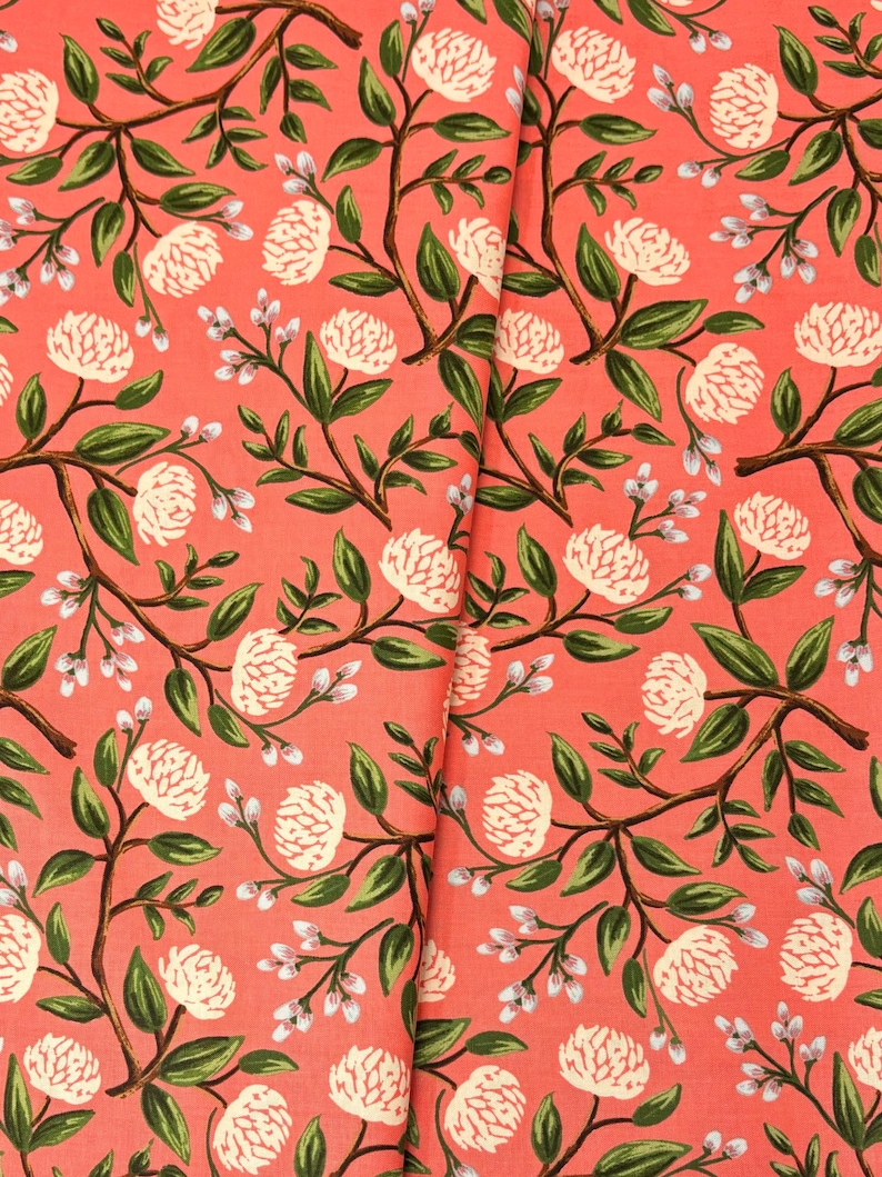May include: Coral pink fabric with a repeating pattern of white flowers and green leaves.