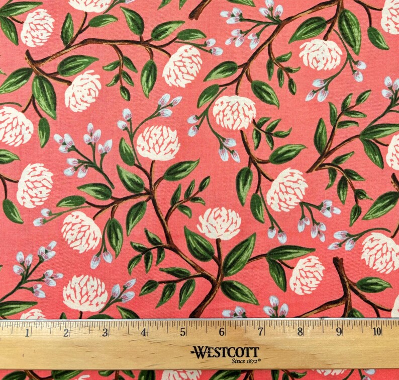 May include: A pink fabric with a white floral pattern. The flowers are stylized peonies with green leaves and stems. A wooden ruler with the text "Westcott Since 1872" is at the bottom of the image.