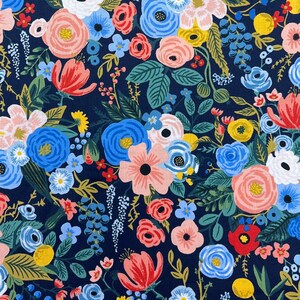 May include: A navy blue fabric with a floral pattern featuring pink, red, blue, and yellow flowers. The fabric is printed with a variety of flowers and leaves, creating a busy and colorful design. The fabric is shown with a ruler, indicating that it is sold by the yard.