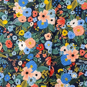 May include: A navy blue fabric with a floral pattern featuring pink, blue, yellow, and red flowers. The fabric is a repeating pattern of flowers and leaves.