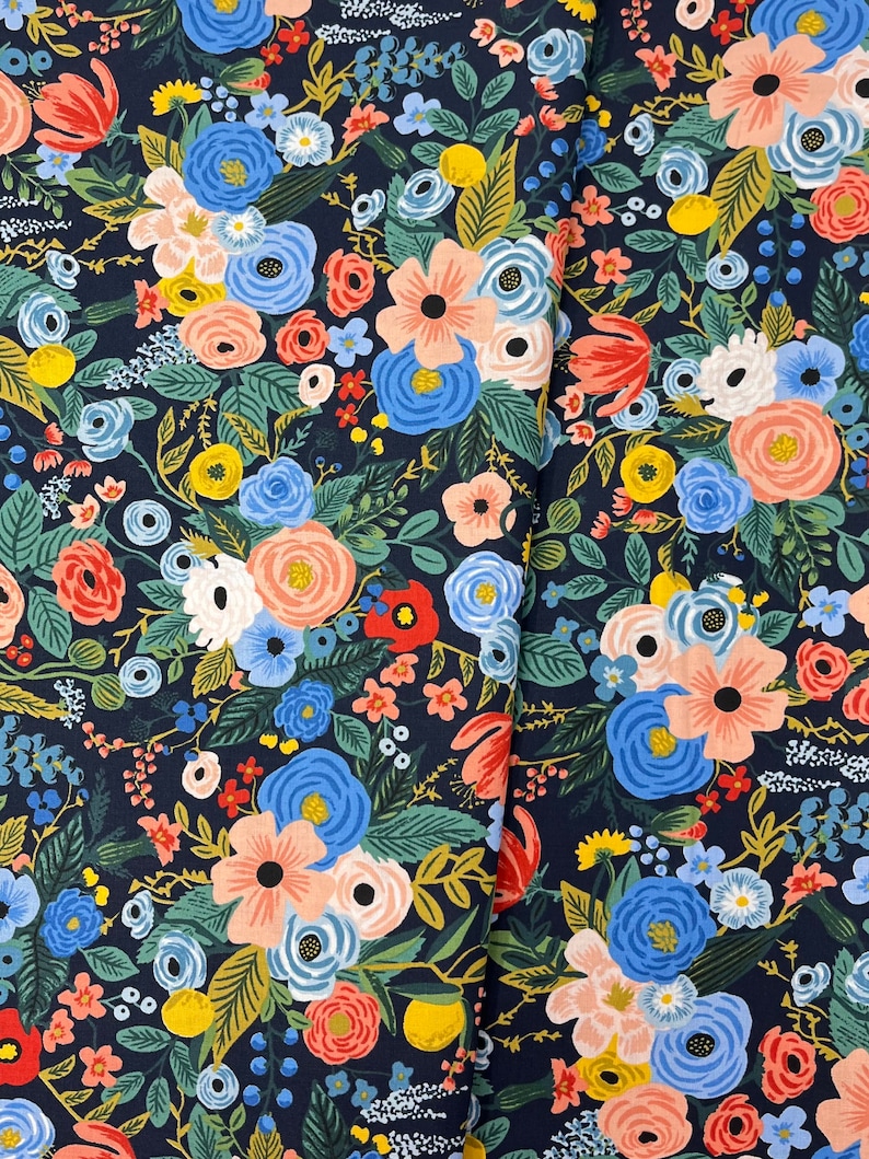 May include: A navy blue fabric with a floral pattern featuring pink, blue, yellow, and red flowers. The fabric is a repeating pattern of flowers and leaves.