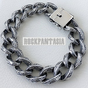 K&ouml;nnte beinhalten: Ein silbernes Kettenarmband mit einem detaillierten, komplizierten Design. Das Armband hat einen Verschluss.