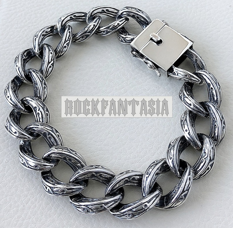 K&ouml;nnte beinhalten: Ein silbernes Kettenarmband mit einem detaillierten, komplizierten Design. Das Armband hat einen Verschluss.