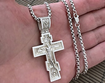Może przedstawiać: Srebrny wisiorek z krzyżem prawosławnym z szczegółowym przedstawieniem Jezusa Chrystusa na łańcuszku typu box chain. Krzyż posiada skomplikowane grawerunki.