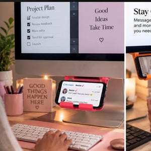 May include: A bright pink and orange plastic smartphone mount designed to attach to the side of a computer monitor. The mount holds a mobile phone in a horizontal position, allowing for screen visibility while working at a desk with a keyboard.