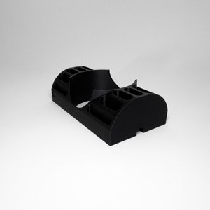 K&ouml;nnte beinhalten: Ein schwarzer, 3D-gedruckter Schreibtisch-Organizer mit mehreren F&auml;chern und einem geschwungenen Design. Der Organizer hat eine rechteckige Basis und abgerundete Enden mit verschiedenen Schlitzen und Abschnitten zur Aufbewahrung von Gegenst&auml;nden.