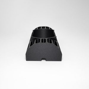 K&ouml;nnte beinhalten: Ein schwarzes, 3D-gedrucktes Objekt mit halbkreisf&ouml;rmiger Basis und vertikalen Schlitzen. Der obere Teil hat ein gebogenes Design mit rechteckigen &Ouml;ffnungen. Das Objekt besteht aus mattem, schwarzem Material.