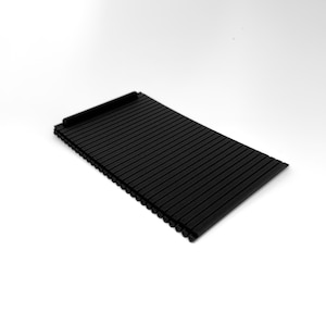 Op de afbeelding: Een zwarte, rechthoekige mat voor de console van de auto met een geribbeld oppervlak. De mat heeft aan één uiteinde een kleine, verhoogde lip. De ribbels lopen evenwijdig aan elkaar over de lengte van de mat. De mat is gemaakt van een textuur.