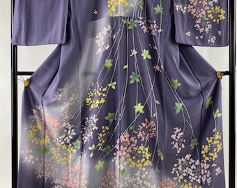 May include: A purple silk kimono with a floral pattern of pink, yellow, and white flowers on a light gray background. The flowers are arranged in a flowing pattern, and the kimono is decorated with green leaves.