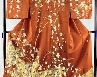 May include: A traditional Japanese kimono with a vibrant orange background and intricate white floral embroidery. The kimono features a delicate floral pattern with gold accents, creating a luxurious and elegant look.