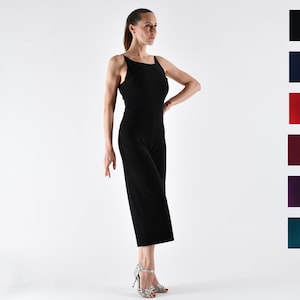 May include: A woman wearing a black sleeveless jumpsuit with a scoop neck. She is standing on a white background and wearing silver heels.