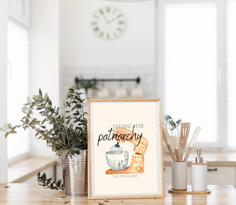May include: A framed print with a watercolor illustration of a kitchen mixer with the text "Feeding the patriarchy" and "Soli Deo Gloria" in black lettering.