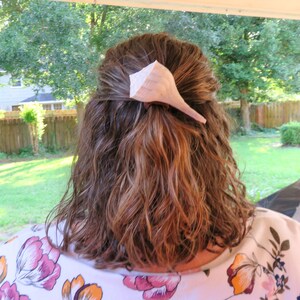 May include: A woman with brown hair is wearing a white shirt with a floral pattern. She has a seashell hair clip in her hair.